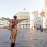 Woman enjoys beautiful view on famous Duomo cathedral in Florence, standing on empty cathedral square during morning time. Stylish woman visiting italian landmarks. Traveling Italy concept