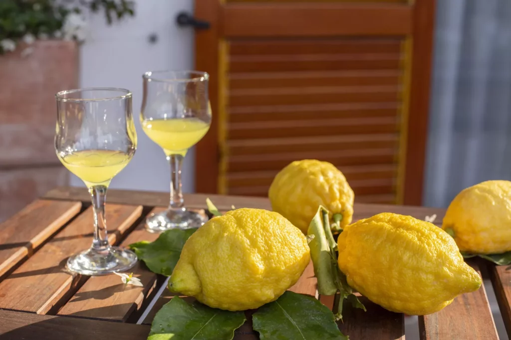 Lemons with leaves, lemonade or limoncello in a glass glass, on a wooden table on the terrace