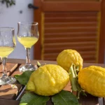 Lemons with leaves, lemonade or limoncello in a glass glass, on a wooden table on the terrace