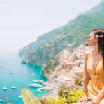 Young woman in yellow dress with Positano village on the background, Amalfi Coast, Italy
