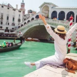 woman sitting near rialto bridge in venice italy looking at grand canal with gondolas summer time copy space