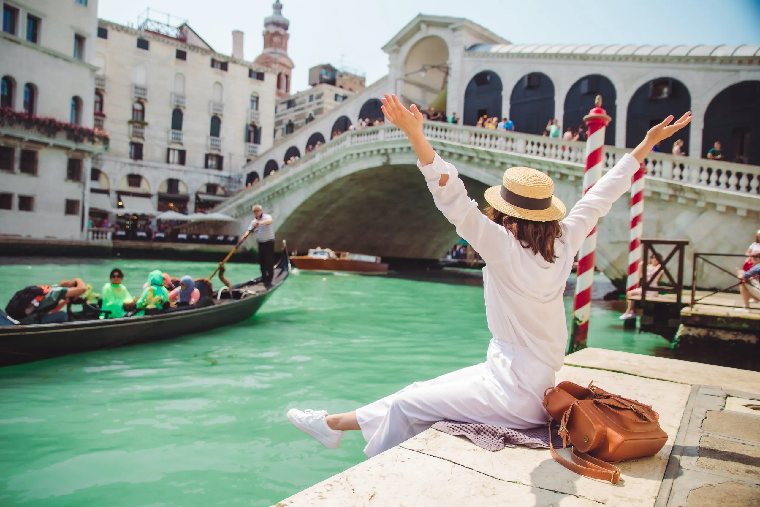 woman sitting near rialto bridge in venice italy looking at grand canal with gondolas summer time copy space